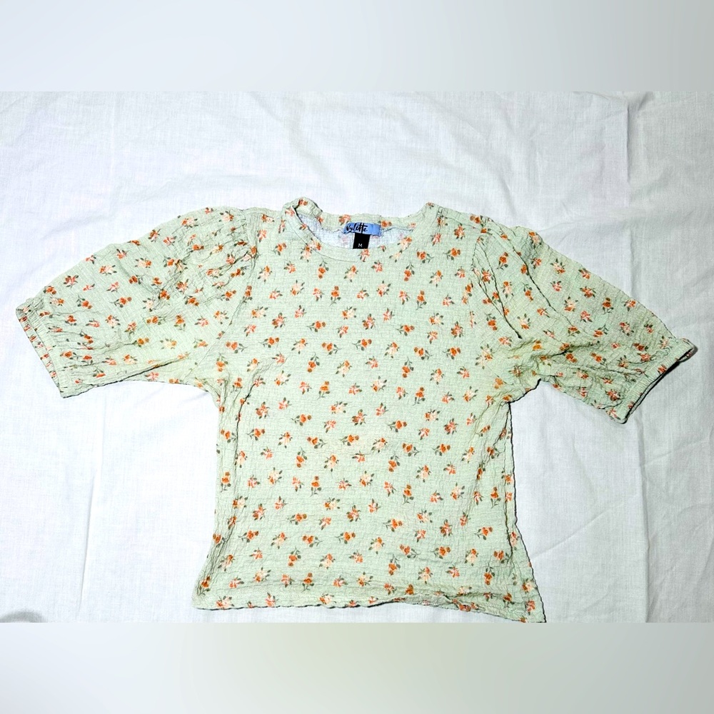 Mint green top with slight puffed sleeves, floral decor and thin material.